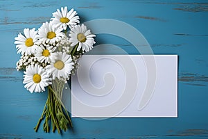 mockup white blank paper sheet with bouquet white daisies flowers top view on blue wooden background, floral template empty card