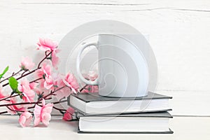 Mockup of a white ceramic mug on a table with books and flowers