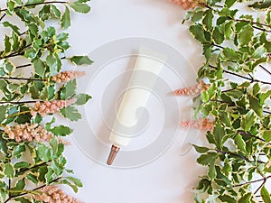 Mockup of white cosmetic tube with long nozzle and bronze screw cap, fresh greens and pink flowers on a white background.