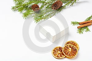 Mockup white gift box with dried orange fruits, cinnamon stick, cone, sprig of spruce Christmas tree on white background.