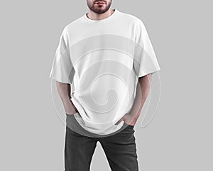 Mockup of white oversized t-shirt on bearded man with hands in pockets of dark jeans, trendy shirt, isolated on background