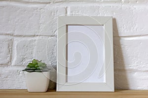 Mockup of a white photo frame and succulents in a vase on a table or shelf