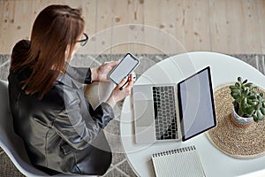 Mockup white screen laptop and mobile phone woman using computer sitting at table at home, top view