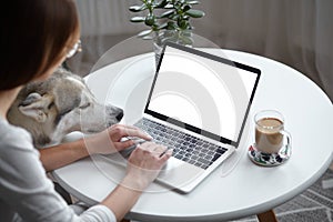 Mockup white screen laptop woman with a pet dog using computer while sitting at table at home, back view