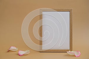 Mockup Wooden frame with Empty white paper blank and delicate pink rose petals on beige background. Minimal trendy