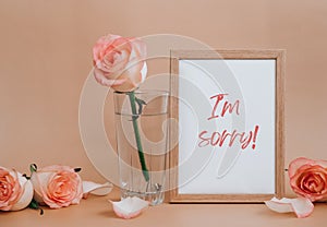 Mockup Wooden frame with text I AM SORRY on blank and delicate pink roses on beige background. Minimal trendy