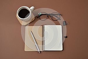 Mockup workspace with office supplies, pen, coffee cup, notepad and glasses on brown background. Flat lay, top view,