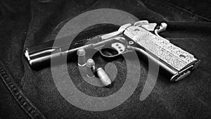 Model 1911 pistol and three cartridges (.45 ACP) on a black denim background, monochrome photo