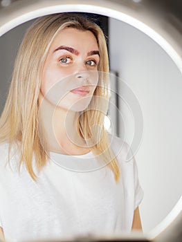 Model with angel eyes looking at camera thru the ring light lamp after microblading procedure