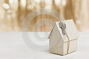 Model of cardboard house with key against bokeh background. house building, loan, real estate or buying a new home photo