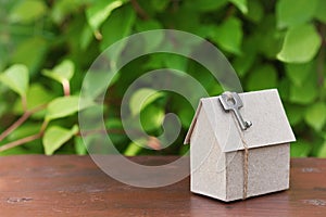 Model of cardboard house with key against green leaves background. Purchase, rent and construction country real estate concept.