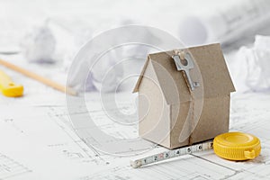 Model cardboard house with key and tape measure on blueprint. Home building, architectural and construction design concept