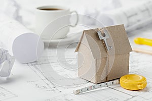 Model cardboard house with key and tape measure on blueprint. Home building, architectural and construction design concept