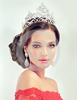 Model in a delicate make up, dressed in a red gown and crown.