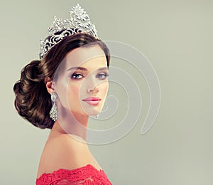 Model in a delicate make up, dressed in a red gown and crown.