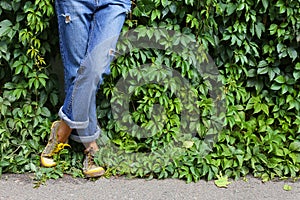 Model in denim pants. Legs. Sport shoes. near a wall overgrown with climbing plants. Background with plant leaves