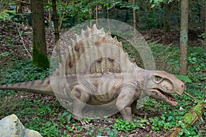 Model of dinosaur dimetrodon from genus nonmammalian synapsids, standing on four legs on grass, on background of trees, side view