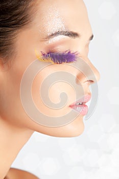 Model with fake eyelashes made of feather side view face glitters on forehead