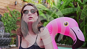 Model in glasses on a pink mattress in the pool. A young woman poses in the tropics. Summer party, joy