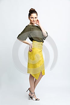 Model in green blouse, yellow suede skirt with yellow belt, white heeled sandals isolated on white background.