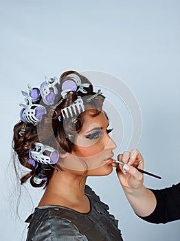 Model with hair in curlers and lipstick brush.