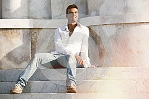 Model handsome man relaxed sitting on the steps of white marble.