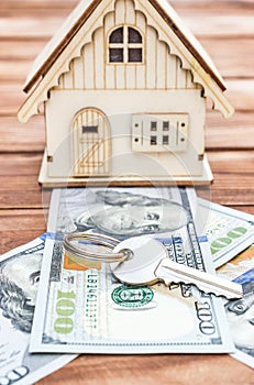 Model of house with dollar bills and key on wooden background