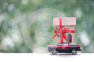 Model house and gift box with red ribbon on miniature car on green background.