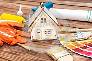 Model of house with paint roller, brushes and color swatches book on the table. Home improvement and repairing concept