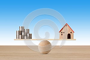 Model house on seesaw balancing with stacking coins money on blue background. Property investment and home mortgage financial real