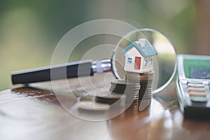 Model house on stack coin , magnifying glass searching for a new home, House searching concept with a magnifying glass