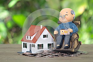 A model of an old man sitting on a rocking chair and a model of a small house on a pile of dollar coins