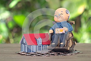 A model of an old man sitting on a rocking chair and a model of a small house on a pile of dollar coins