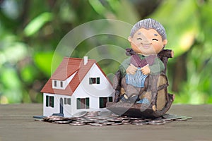 A model of an old woman sitting on a rocking chair and a model of a small house on a pile of dollar coins