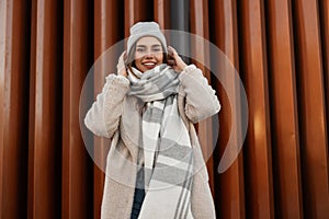 Model of a positive young woman with a beautiful smile in fashionable faux fur coat in a knitted stylish hat with a woolen plaid
