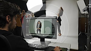 Model and production team in the studio. Full length woman model poses for photographer on set, editor checks photos on