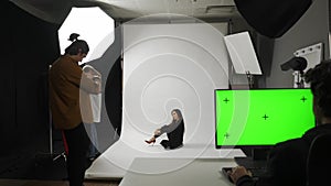 Model and production team in the studio. Full length woman model poses for photographer on set, editor monitor chroma