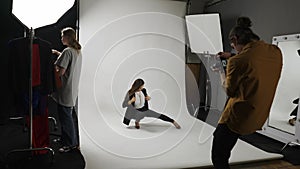 Model and production team in the studio. Full length woman model poses for photographer on set, girl stylist picks