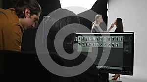 Model and production team in the studio. Retouch and photographer talking checking photos looking at monitor, assistant