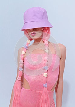 Model 90s party hip-hop style posing in white studio. Trendy pink jumpsuit, bucket hat and pink hair. Fashion unicorn Lady vibes