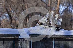 Model of a sailboat in the snow on a wooden fence