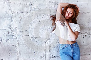 Model tests. Beautiful redhead girl with curly hair.Natural color. Stands with long hair blowing against the light brick