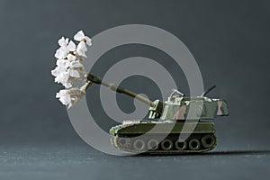 Model toy of battle tank firing flowers from the barrel. Peace and no war concept. Military pancer on the gray background