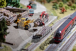 A model of a toy electric train drives along the rails past a sorting and freight station with firewood and wagons