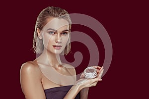 Model wearing open shoulder top holding face cream