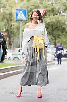 Model wearing a pair of silver pants, a shirt with a yellow backpack attached and a pair of pink heeled shoes