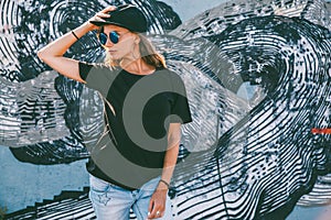 Model wearing plain tshirt and sunglasses posing over street wall