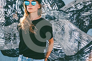 Model wearing plain tshirt and sunglasses posing over street wall