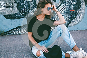 Model wearing plain tshirt and sunglasses posing over street wall