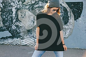 Model wearing plain tshirt and sunglasses posing over street wall